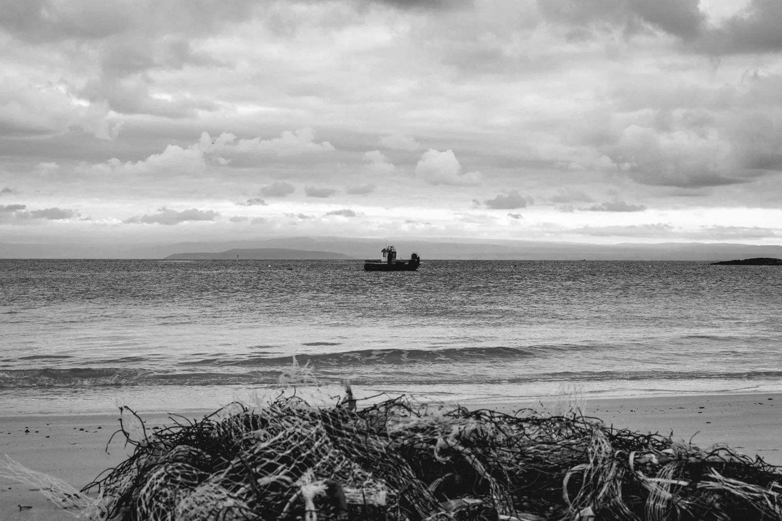 Boat on the horizon beyond a heap of dried seaweed