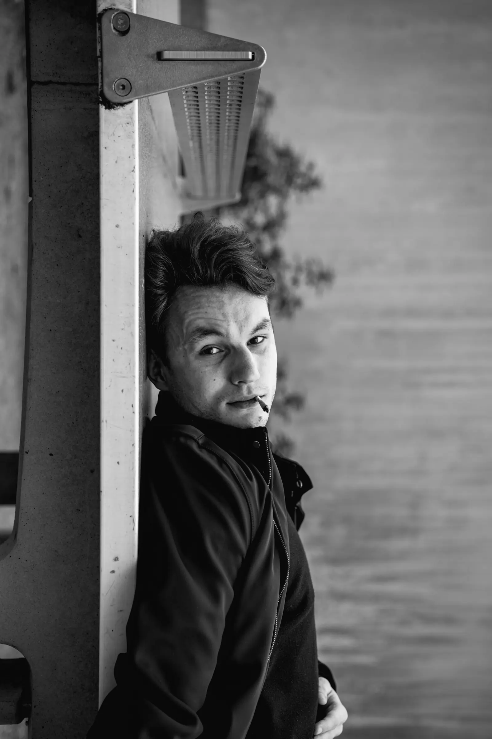 Man with a cigarette leaning against a window frame, in black and white