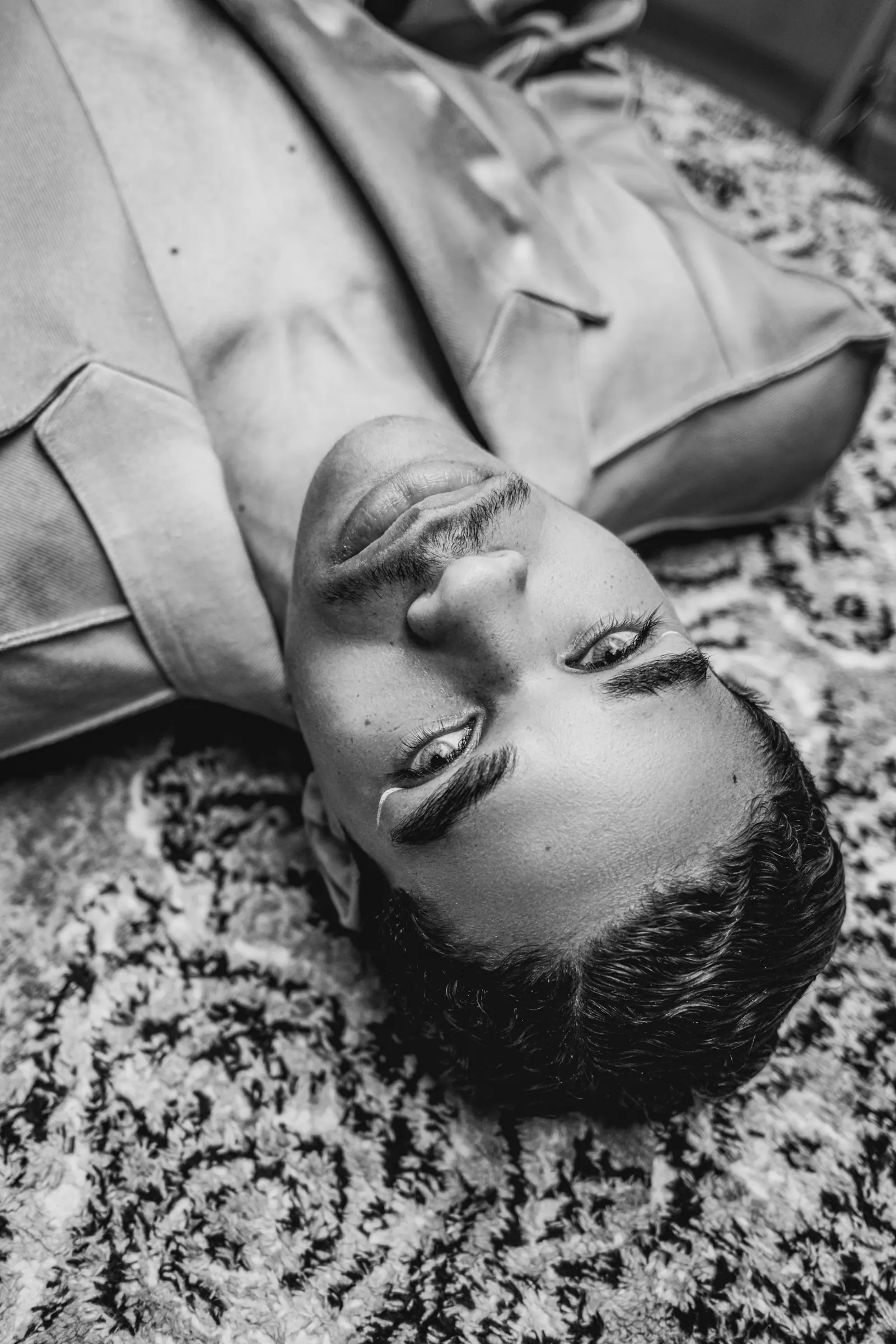 Man lying on a patterned rug, seen from above, in black and white