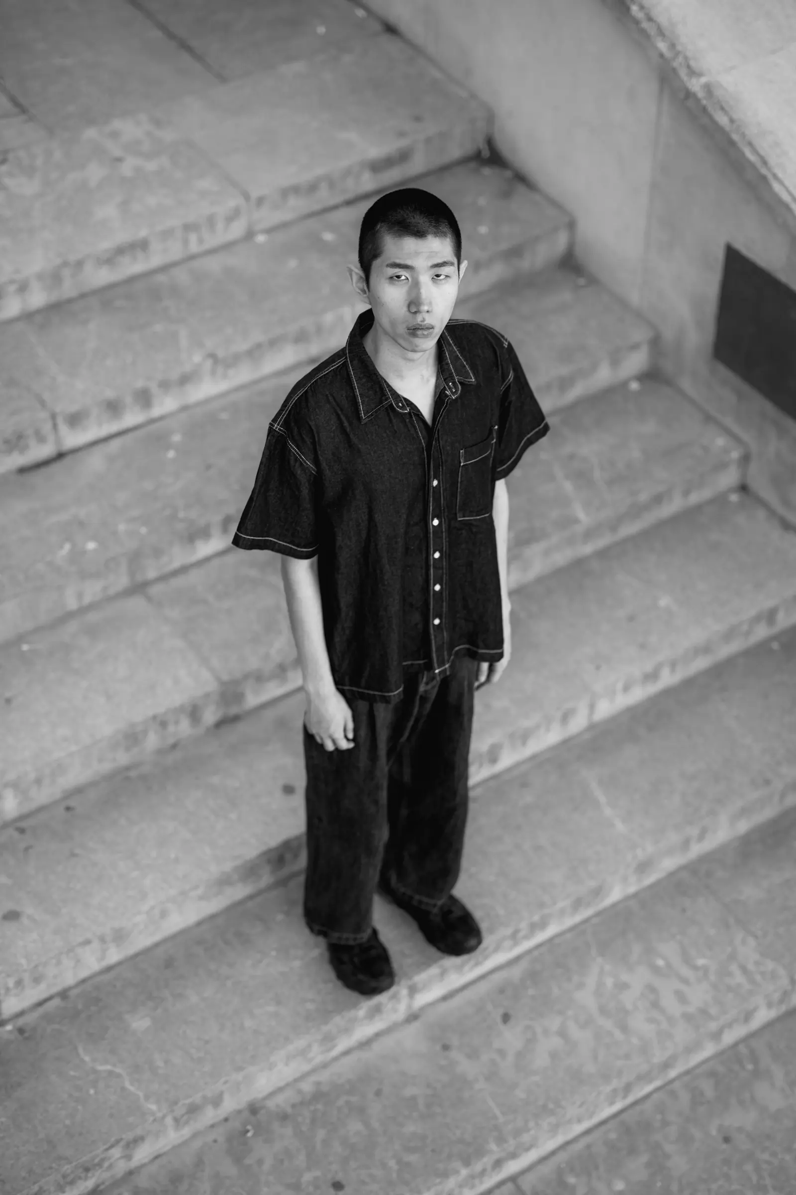 Young man in a dark shirt standing on stone steps, seen from above, in black and white
