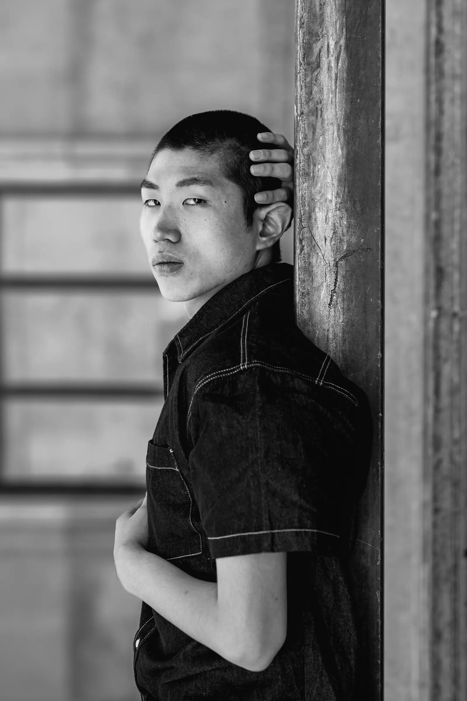 Young man leaning against a stone column, a hand on his head, in black and white