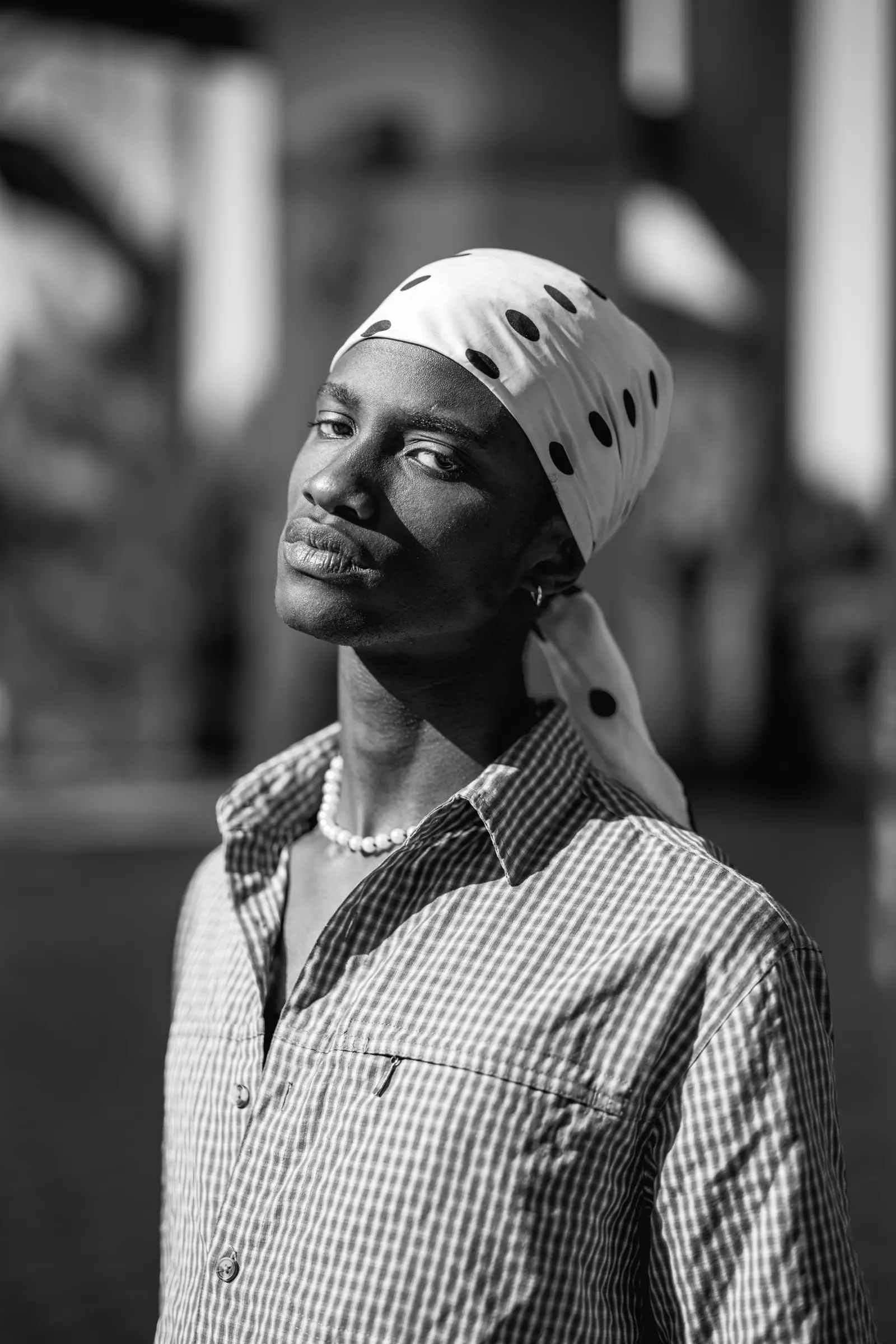 Man in a patterned headscarf and a pearl necklace, in black and white