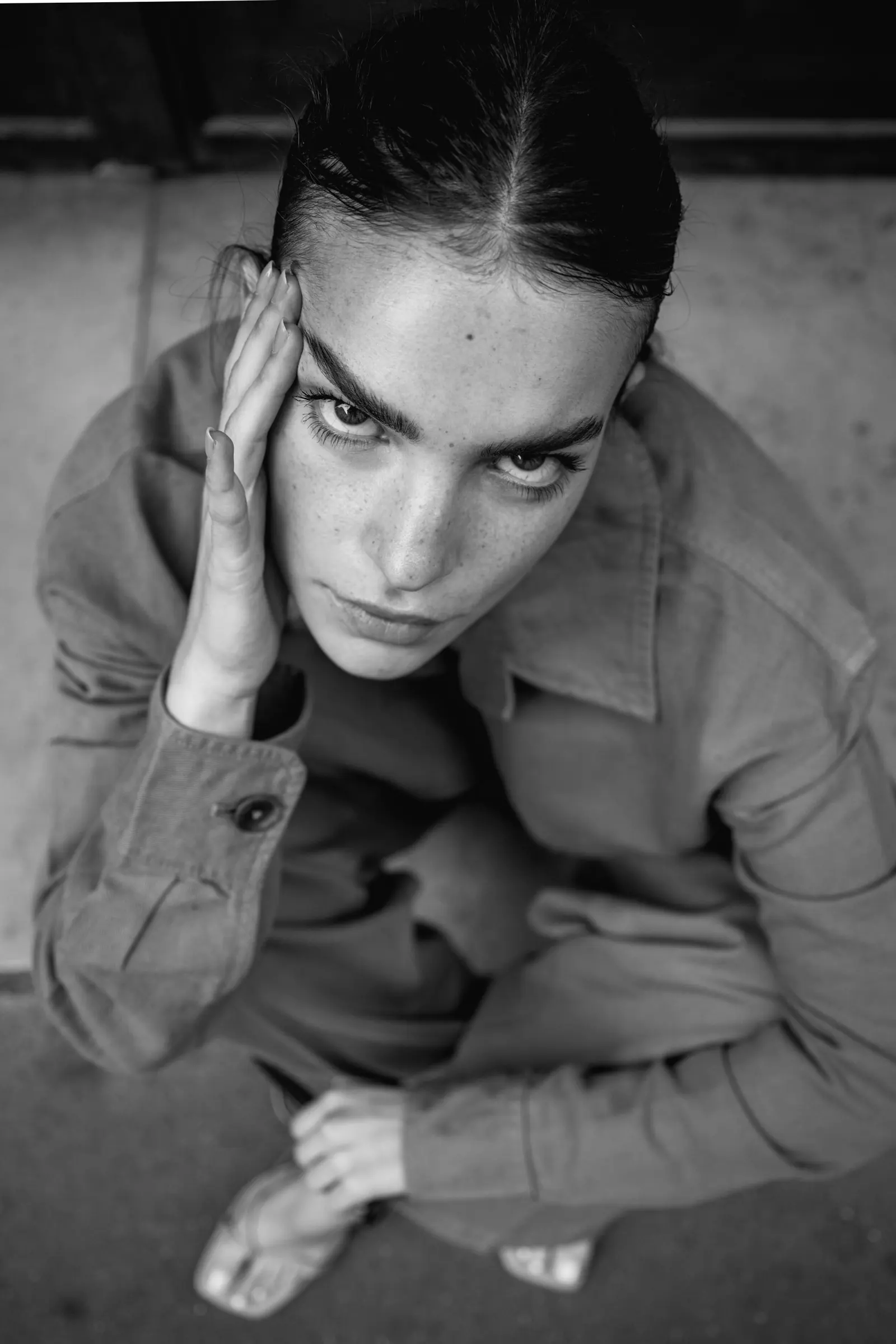 Woman crouching with a hand against her temple, looking up, in black and white