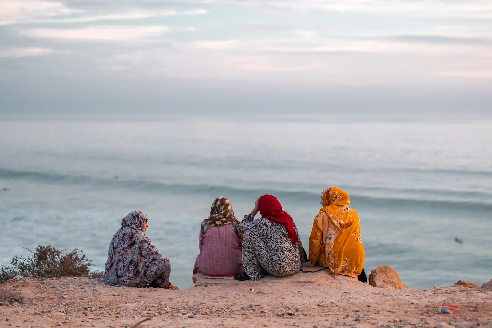 Four women in coloured veils sitting above the ocean