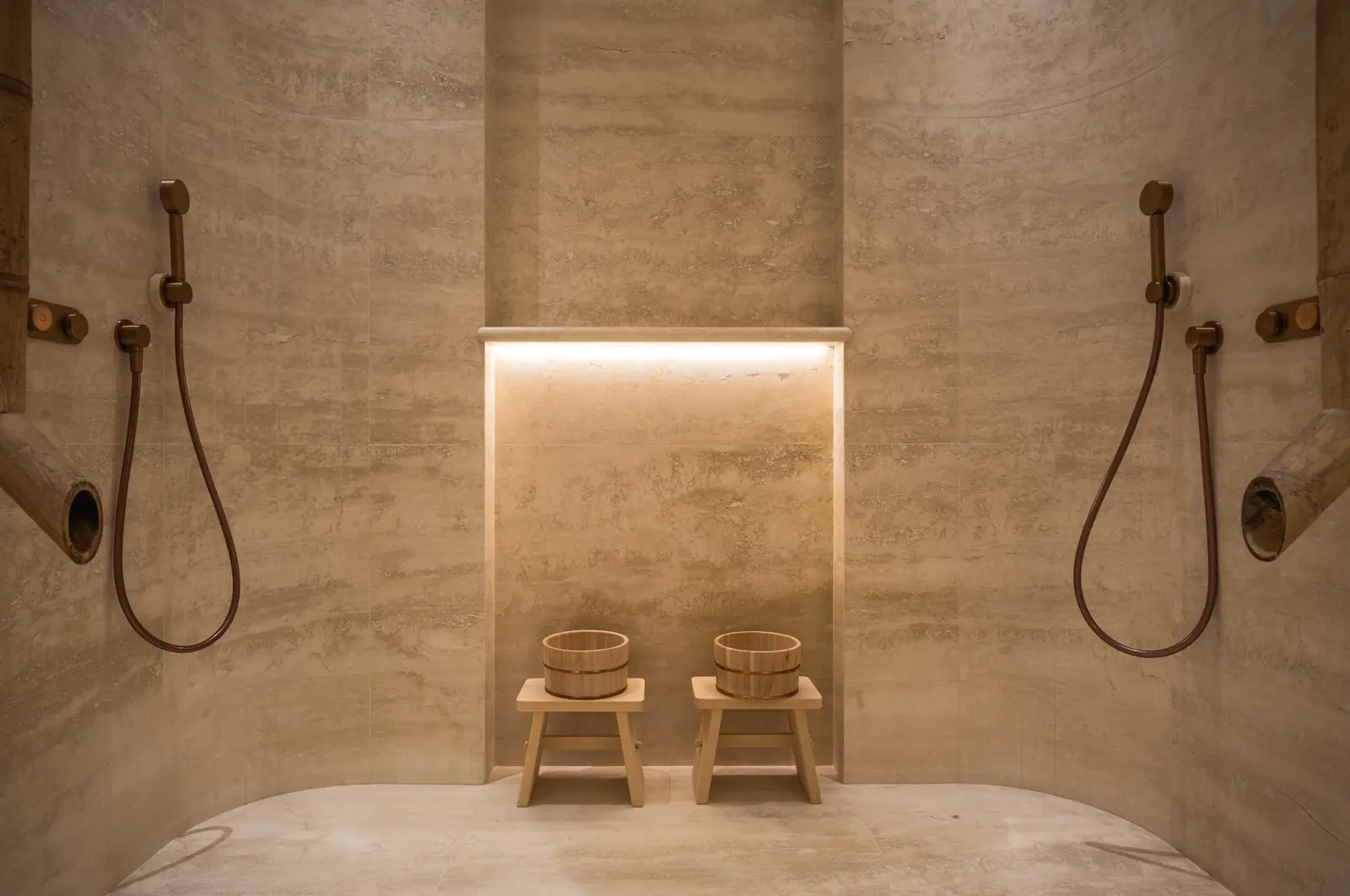 Twin showers in a travertine wall with two wooden stools