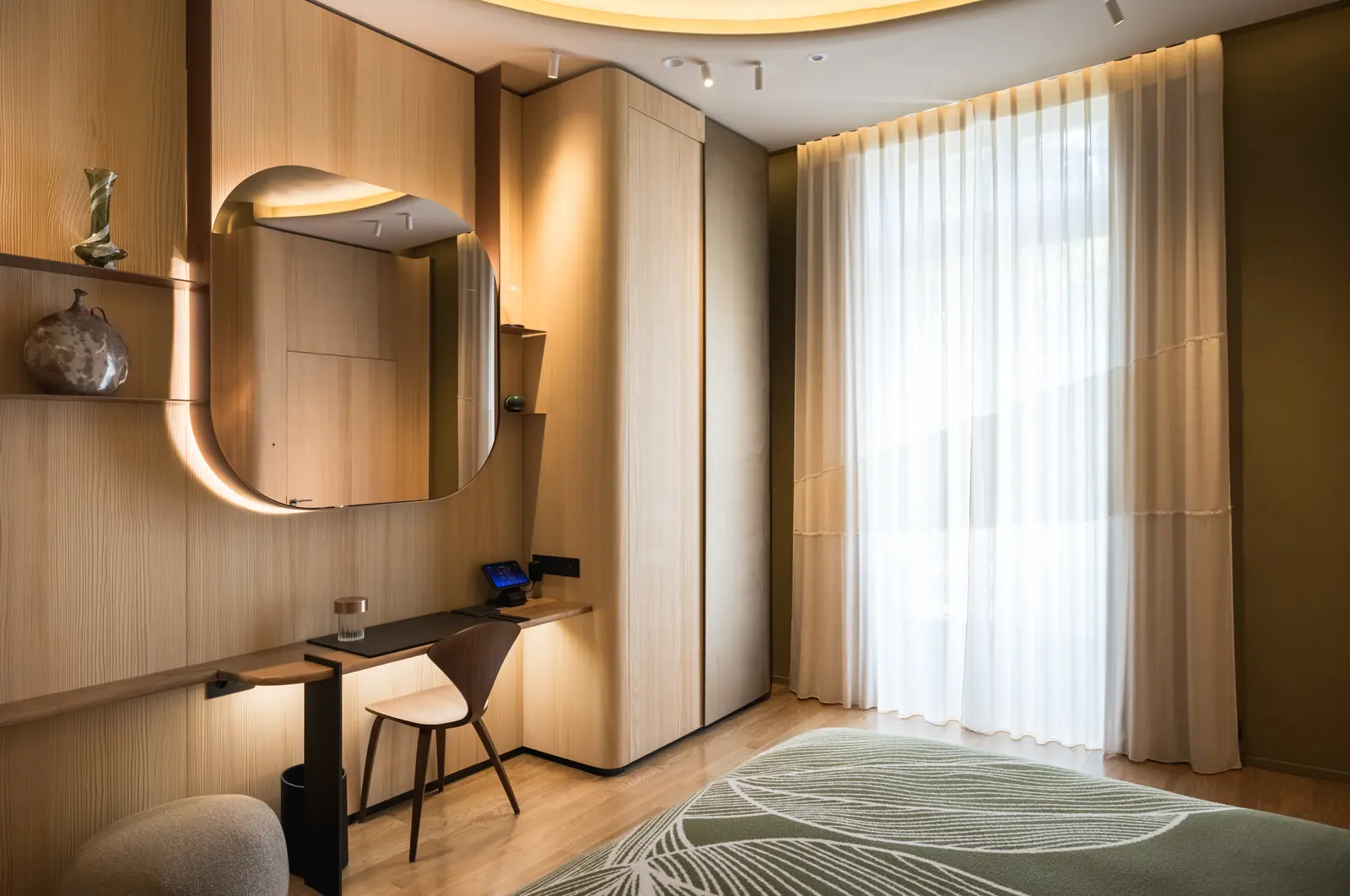 Guest room at Le Dix with an oak desk, a rounded mirror and sheer curtains