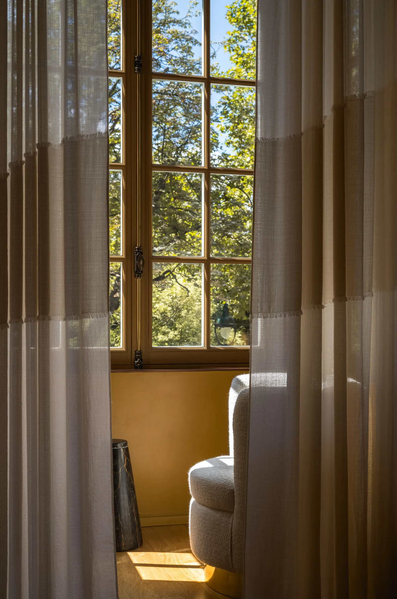 Tall window with linen curtains and a white armchair