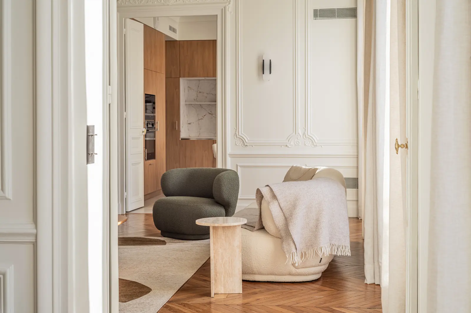Green bouclé armchair and a white sofa with a wool throw, the oak kitchen through the doorway