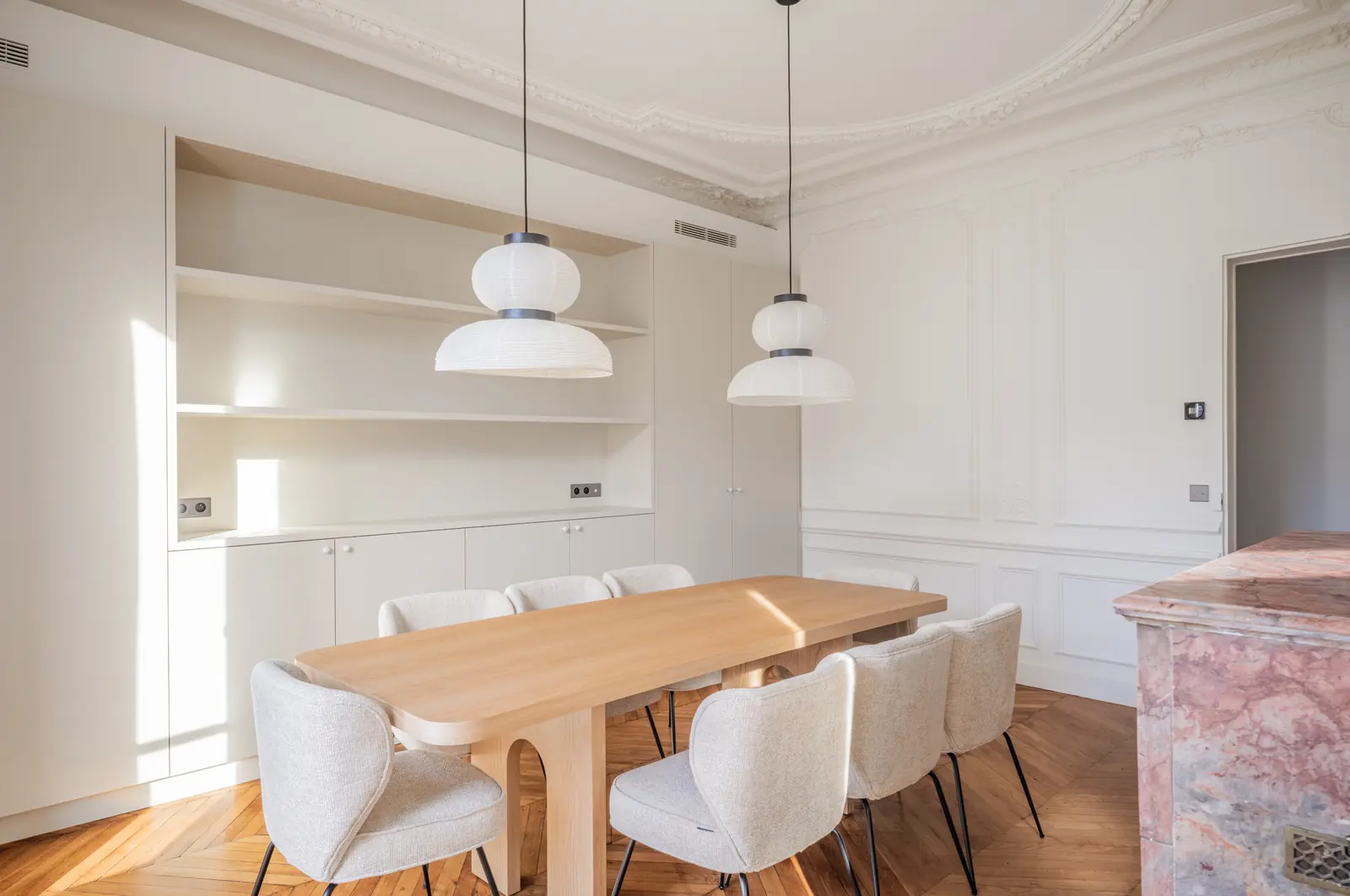 Dining table with pendant lamps under a moulded ceiling